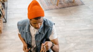 Male retail employee in orange beanie hanging clothes on rack
