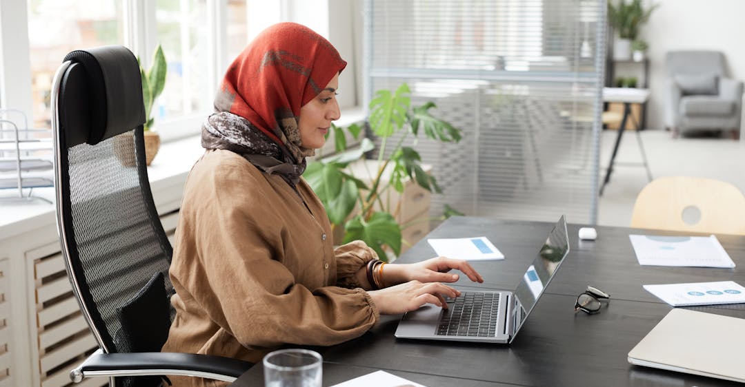 Woman in hijab at desk using laptop for online background check and background screening in the Middle East