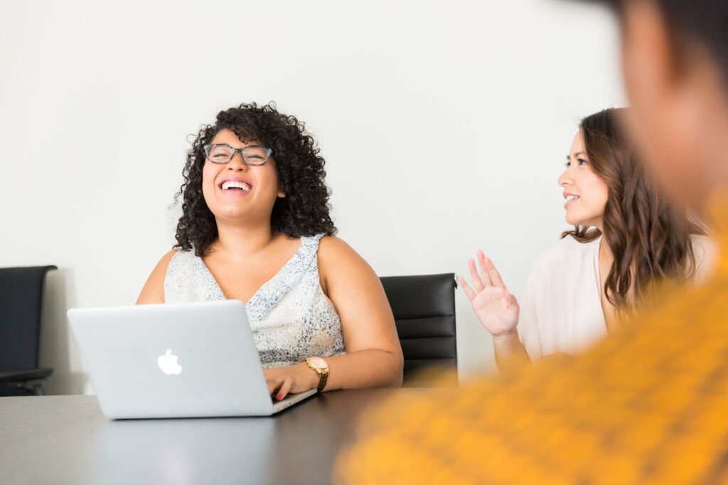 Woman in White HR Recruiter Dress in Front of Silver Macbook Laughing with Colleagues